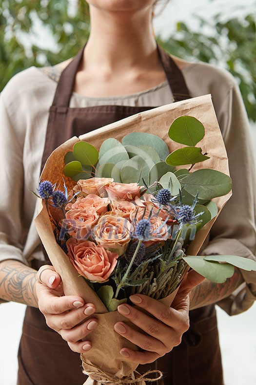 Florist woman with a bouquet of coral roses and green leaf. Girl is holding a flowers in her hands. The gift to Mother's Day. Florist woman with a bouquet of coral roses and green leaf. Girl is holding a flowers in her hands. The gift to Mother's Day.