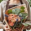 Florist woman with a bouquet of coral roses and green leaf. Girl is holding a flowers in her hands. The gift to Mother's Day.