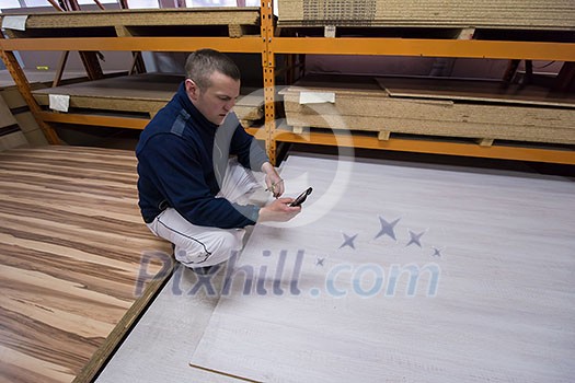 young man carpenter using a mobile phone to calculate measures for wooden board while working in big modern carpentry High quality wood concept young man carpenter using a mobile phone to calculate measures for wooden board while working in big modern carpentry High quality wood concept