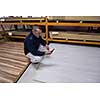young man carpenter using a mobile phone to calculate measures for wooden board while working in big modern carpentry High quality wood concept