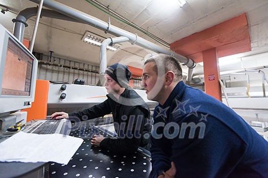 two young carpenters calculating and programming a cnc wood working machine in workshop. wood workers preparing a computer program for CNC machine at big modern carpentry two young carpenters calculating and programming a cnc wood working machine in workshop. wood workers preparing a computer program for CNC machine at big modern carpentry
