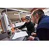 two young carpenters calculating and programming a cnc wood working machine in workshop. wood workers preparing a computer program for CNC machine at big modern carpentry
