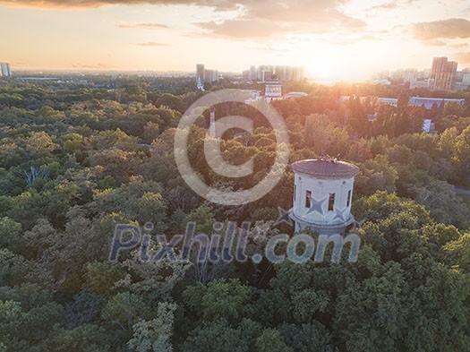 A city in the distance and a green park with a tower and people on the roof against the sky with the sunset. Aerial view from the drone A city in the distance and a green park with a tower and people on the roof against the sky with the sunset. Aerial view from the drone