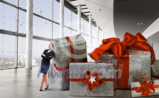 Young businesswoman among pile of gift boxes. Mixed media Young businesswoman among pile of gift boxes. Mixed media
