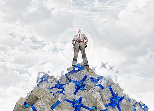 Young businessman among pile of gift boxes. Mixed media Young businessman among pile of gift boxes. Mixed media