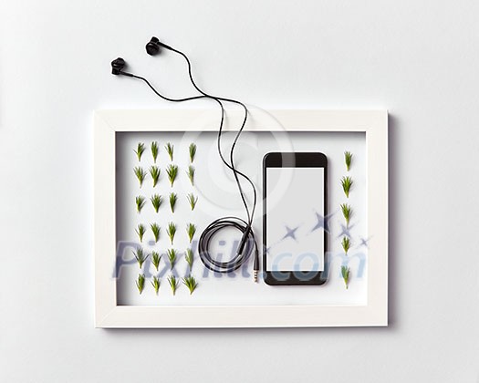 Creative ogranic herbal pattern of pine needles twigs, mobile smartphone with blank screen for mockup and headphones in a frame on a light gray background. Place for text. Flat lay. Creative ogranic herbal pattern of pine needles twigs, mobile smartphone with blank screen for mockup and headphones in a frame on a light gray background. Place for text. Flat lay.