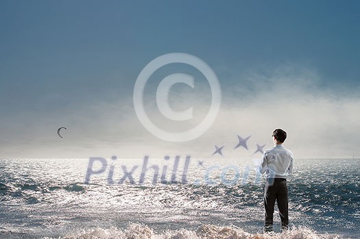 Young relaxed businessman at seaside looking far away at sea. Mixed media Young relaxed businessman at seaside looking far away at sea. Mixed media