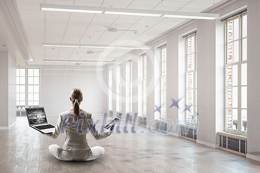 Young businesswoman in lotus pose on office floor. Mixed media Young businesswoman in lotus pose on office floor. Mixed media