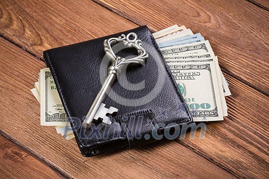 Dollar banknotes in leather purse and old vintage key on wooden table Dollar banknotes in leather purse and old vintage key on wooden table