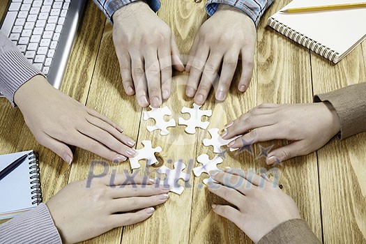 Group of people sitting at table and assembling jigsaw puzzle Group of people sitting at table and assembling jigsaw puzzle