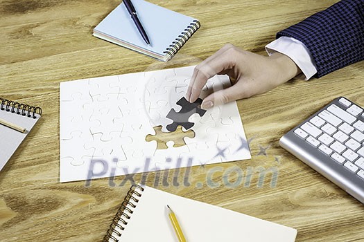 Hand of businesswoman completing puzzle with missing piece Hand of businesswoman completing puzzle with missing piece