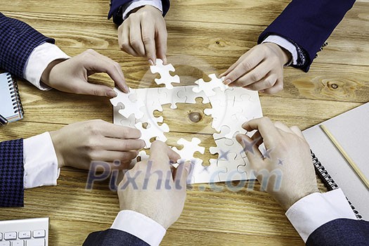 Group of business people sitting at table and assembling jigsaw puzzle Group of business people sitting at table and assembling jigsaw puzzle