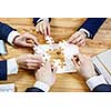 Group of business people sitting at table and assembling jigsaw puzzle