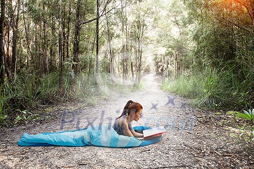 Young woman lying in sleeping bag in forest. Mixed media Young woman lying in sleeping bag in forest. Mixed media