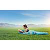 Young woman lying in sleeping bag lying on green grass. Mixed media