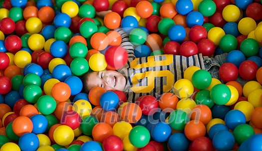 young happy boy having fun while playing and hiding in pool with colorful balls at childrens playroom young happy boy having fun while playing and hiding in pool with colorful balls at childrens playroom