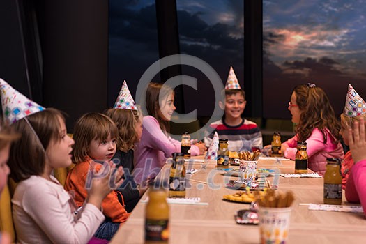 young happy boy and group of his friends having birthday party with a night sky through the windows in the background young happy boy and group of his friends having birthday party with a night sky through the windows in the background