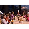 young happy boy and group of his friends having birthday party with a night sky through the windows in the background