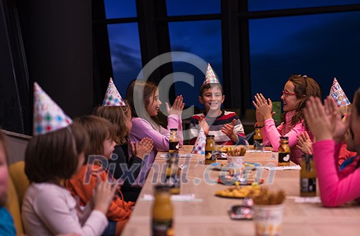 young happy boy and group of his friends having birthday party with a night sky through the windows in the background young happy boy and group of his friends having birthday party with a night sky through the windows in the background