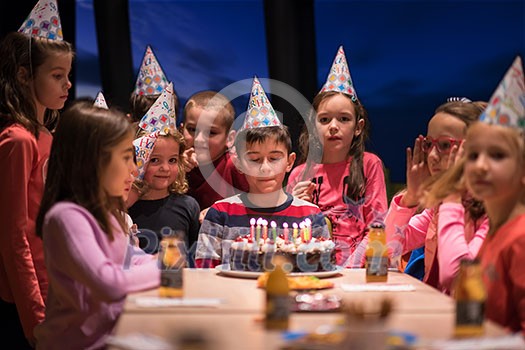 young happy boy and group of his friends having birthday party with a night sky through the windows in the background young happy boy and group of his friends having birthday party with a night sky through the windows in the background