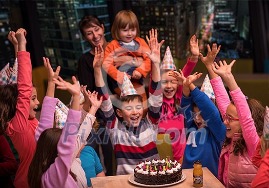 young happy boy and group of his friends having birthday party with a night city through the windows in the background young happy boy and group of his friends having birthday party with a night city through the windows in the background