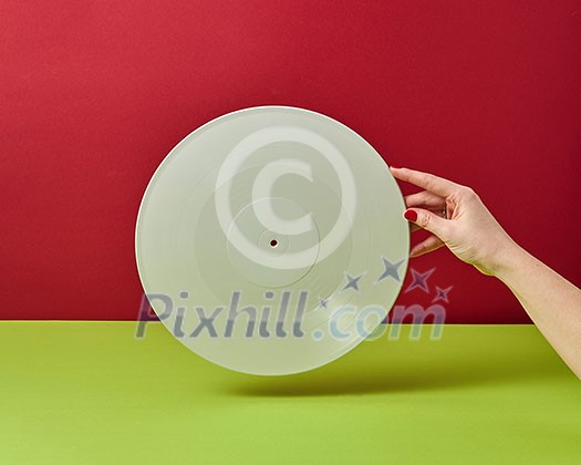 Woman's hand with a manicure holds a retro vinyl record on a duotone background with space for text. Woman's hand with a manicure holds a retro vinyl record on a duotone background with space for text.