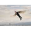 Cheerful businessman with paper wings flying in sky. Mixed media