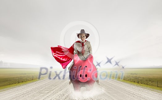 Young businesswoman in red cape riding on piggy bank. Mixed media Young businesswoman in red cape riding on piggy bank. Mixed media