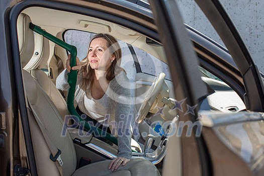 Pretty, middle aged woman vacuum cleaning the interior of a luxury car Pretty, middle aged woman vacuum cleaning the interior of a luxury car