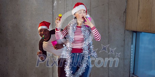 multiethnic business couple wearing red hats while celebrating new year party in new unfinished startup office with a gray wall behind them