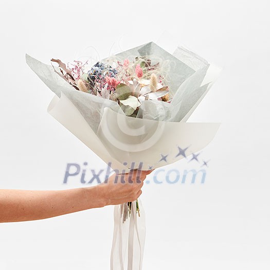 Woman's hand holds congratulation bunch from beautiful flowers on a light grey background, with copy space. Wedding bouquet concept. Woman's hand holds congratulation bunch from beautiful flowers on a light grey background, with copy space. Wedding bouquet concept.