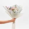 Woman's hand holds congratulation bunch from beautiful flowers on a light grey background, with copy space. Wedding bouquet concept.