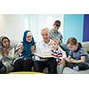 modern muslim family grandparents with grandchildren reading Quran and praying together on the sofa before iftar dinner during a ramadan feast at home