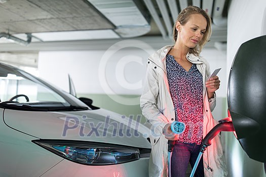 Young woman charging an electric vehicle in an underground garage equiped with e-car charger. Car sharing concept. Young woman charging an electric vehicle in an underground garage equiped with e-car charger. Car sharing concept.