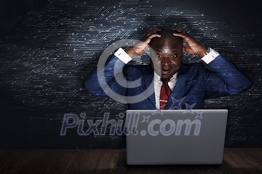 Handsome afroamerican businessman sitting at desk and working on laptop. Mixed media Handsome afroamerican businessman sitting at desk and working on laptop. Mixed media