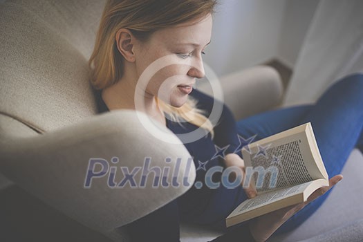 Cute young woman reading a book in a designer chair - color toned image, shallow DOF Cute young woman reading a book in a designer chair - color toned image, shallow DOF