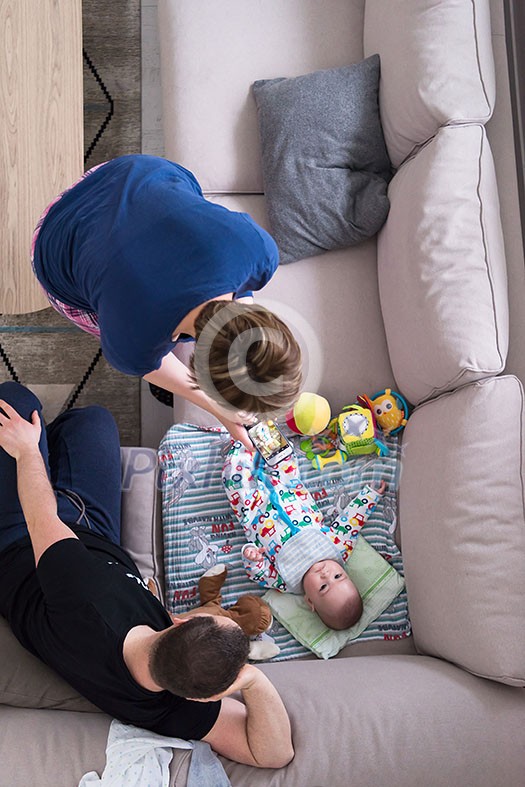 family, technology and people concept -top view of happy mother and father taking picture of baby boy with smartphone on the sofa at home family, technology and people concept -top view of happy mother and father taking picture of baby boy with smartphone on the sofa at home