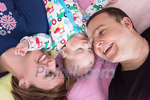Top view of smiling young couple lying together with their adorable baby boy on blankets in their living room at home Top view of smiling young couple lying together with their adorable baby boy on blankets in their living room at home