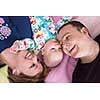 Top view of smiling young couple lying together with their adorable baby boy on blankets in their living room at home