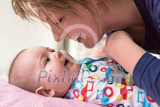 Happy young mother kissing her cute little baby while playing first games on the pink bed at home Happy young mother kissing her cute little baby while playing first games on the pink bed at home