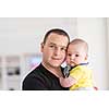 portrait of happy young father holding newborn baby boy near the window at home