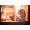 outside view of happy little cute girl playing near the window during winter time at home