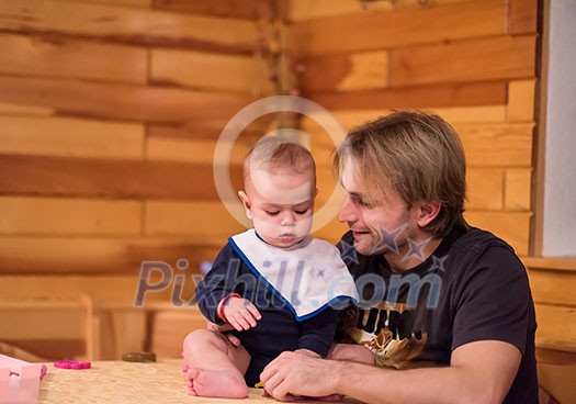 Father and son happy moments Portrait of young father and his cute baby son playing together on table while spending time together at home Father and son happy moments Portrait of young father and his cute baby son playing together on table while spending time together at home