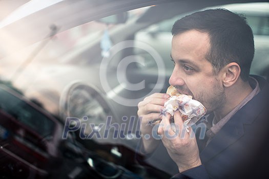 Handsome young man eating a hurried lunch in his car (color toned image; shallow DOF) Handsome young man eating a hurried lunch in his car (color toned image; shallow DOF)