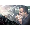 Handsome young man eating a hurried lunch in his car (color toned image; shallow DOF)