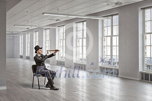 Young businessman wearing cylinder in chair looking in spyglass Young businessman wearing cylinder in chair looking in spyglass