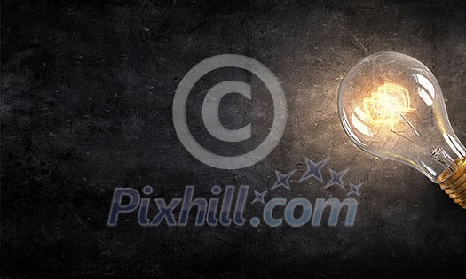 Power and energy concept with glass glowing light bulb on concrete backdrop Power and energy concept with glass glowing light bulb on concrete backdrop