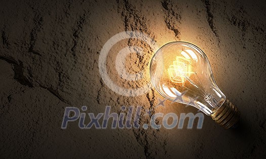Power and energy concept with glass glowing light bulb on concrete backdrop Power and energy concept with glass glowing light bulb on concrete backdrop