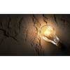 Power and energy concept with glass glowing light bulb on concrete backdrop