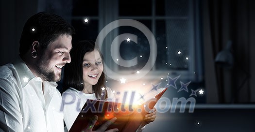 Young father and daughter read book and light coming out of pages